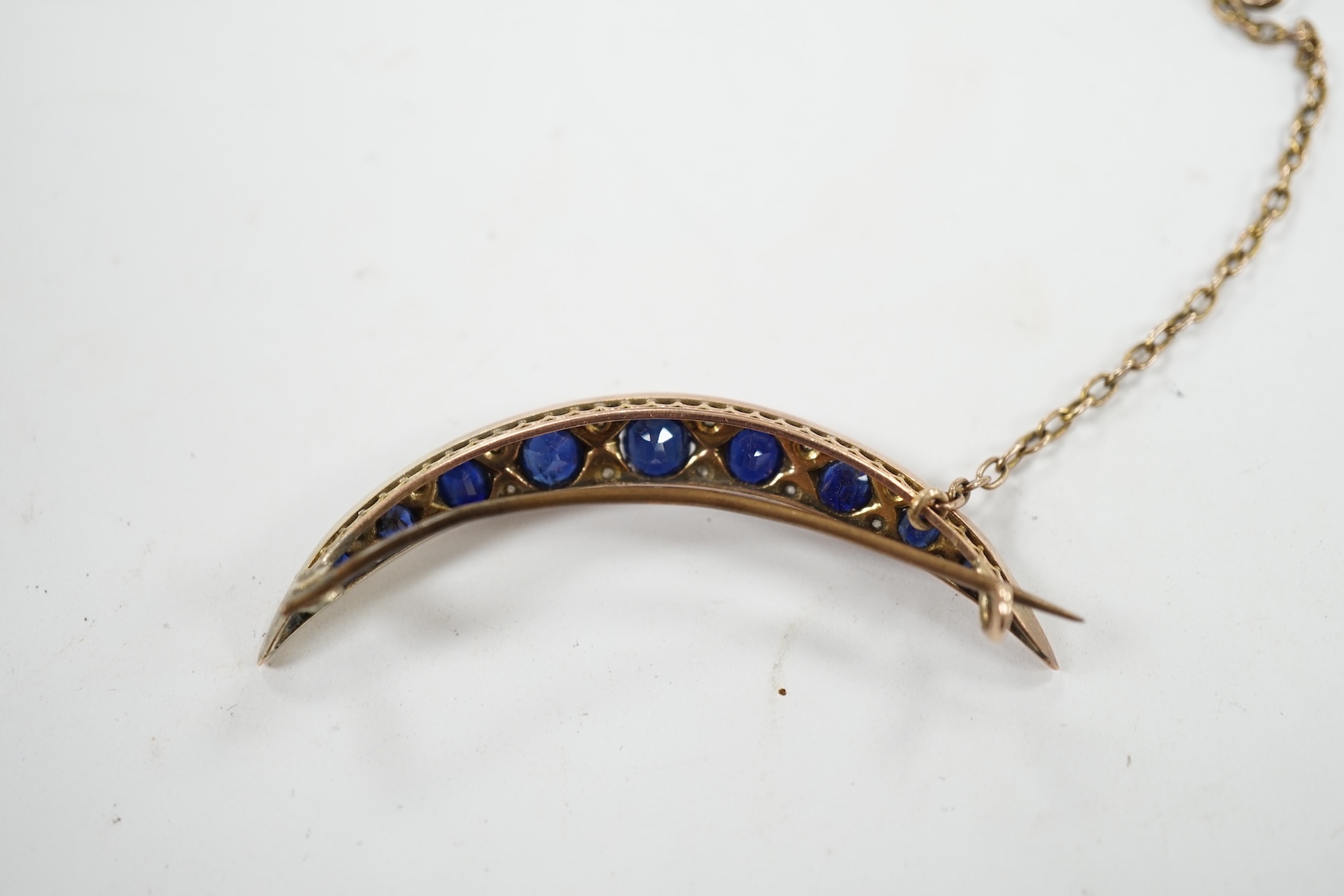 An early 20th century yellow metal, graduated sapphire set crescent brooch, with diamond chip spacers, 49mm, gross weight 5.8 grams. Condition - fair to good